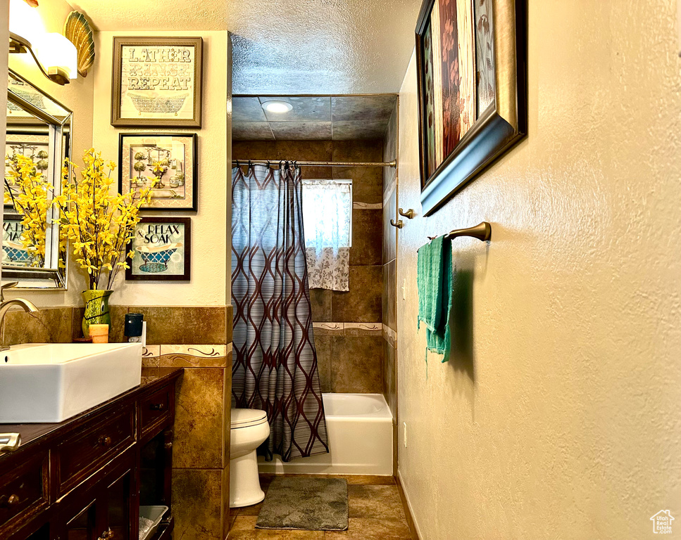 Bathroom with toilet, shower / tub combo with curtain, a textured wall, and vanity