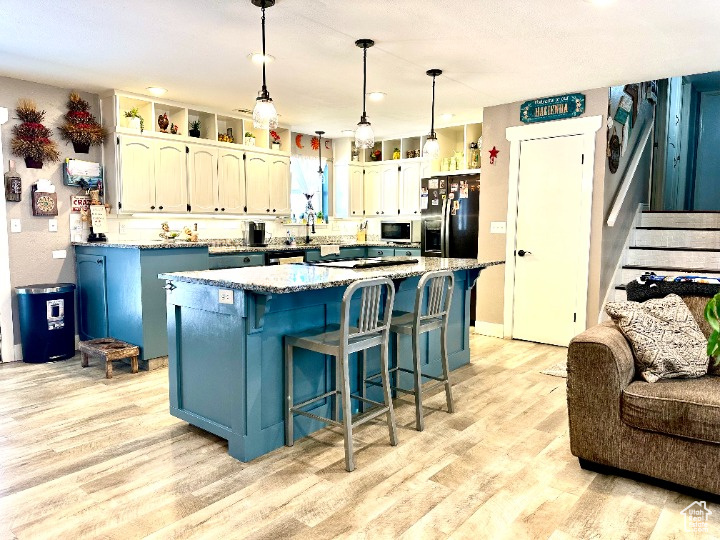 Kitchen featuring white microwave, blue cabinetry, black fridge, and light wood-style floors