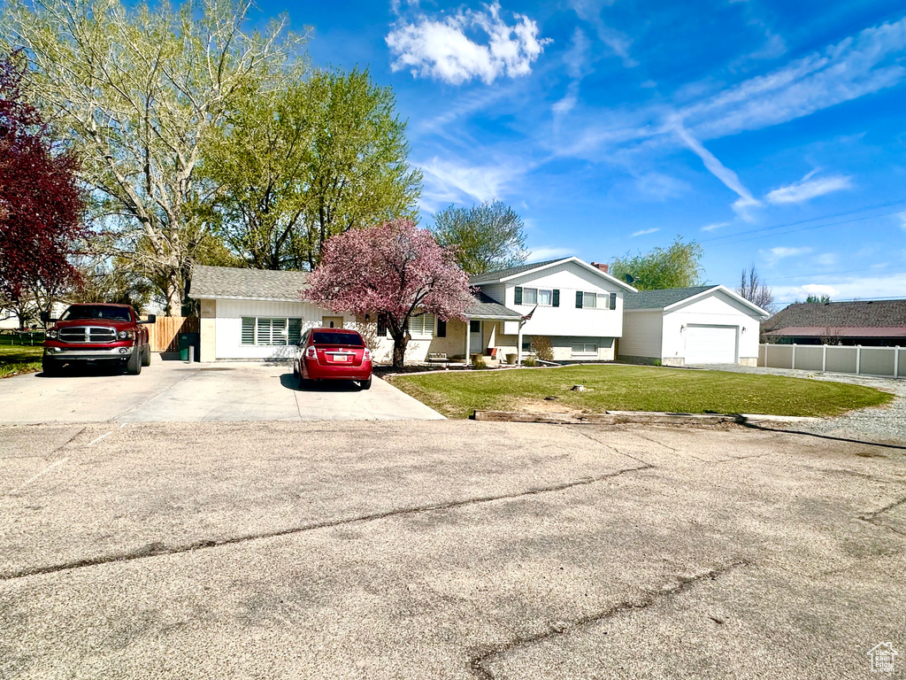 Split level home featuring fence, concrete driveway, a front yard, and a garage
