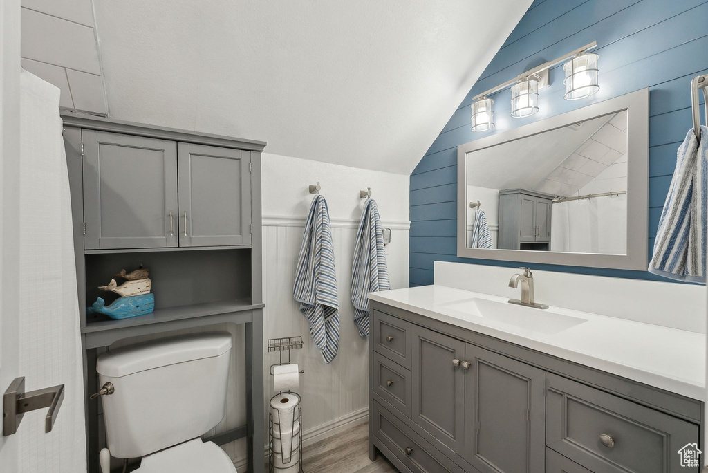 Full bath featuring wooden walls, toilet, wood finished floors, vaulted ceiling, and vanity