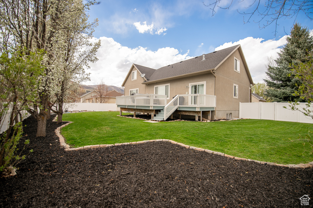Rear view of property featuring a lawn, a wooden deck, a shingled roof, and a fenced backyard
