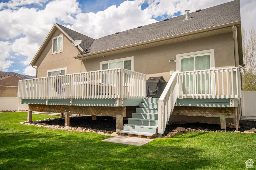 Back of property with a deck, stucco siding, a yard, stairway, and roof with shingles