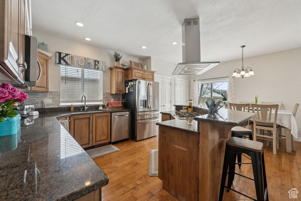 Kitchen with a kitchen island, decorative light fixtures, island exhaust hood, stainless steel appliances, and a sink