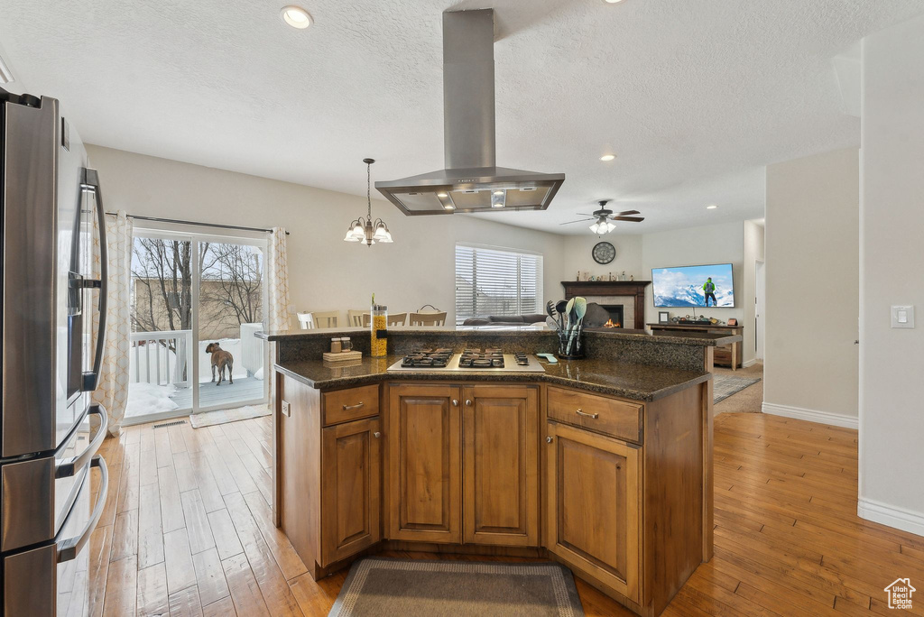 Kitchen featuring an island with sink, stainless steel fridge with ice dispenser, brown cabinetry, and island range hood