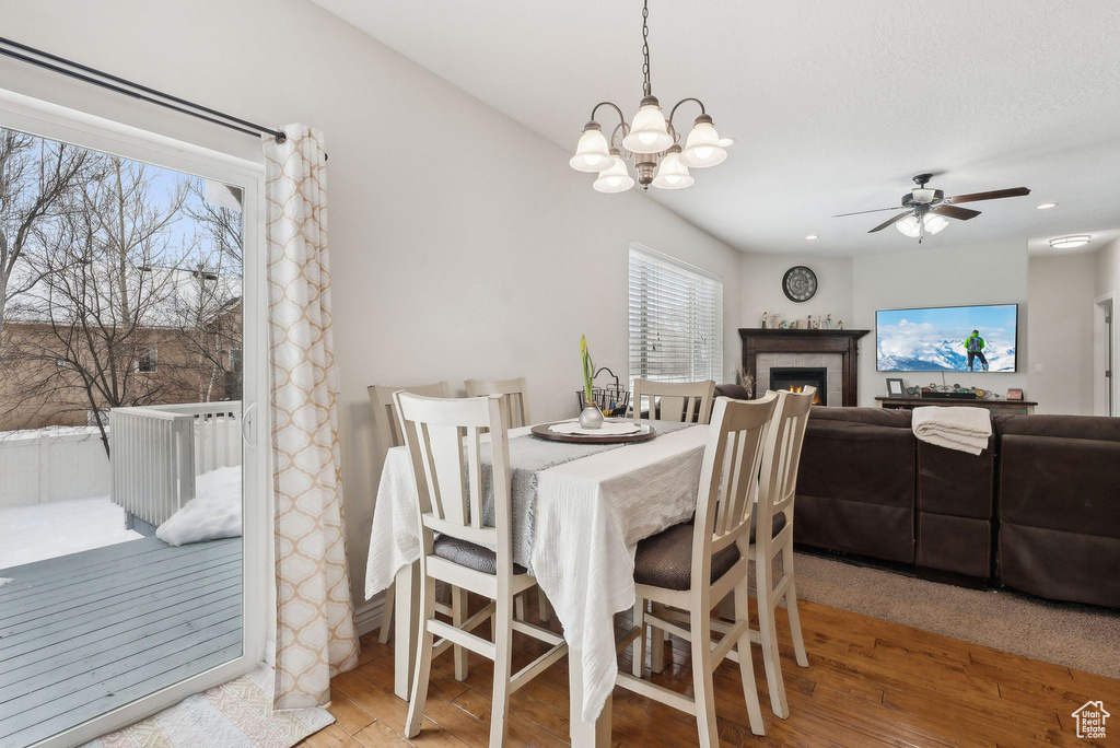 Dining space featuring ceiling fan with notable chandelier, a tiled fireplace, wood finished floors, and recessed lighting