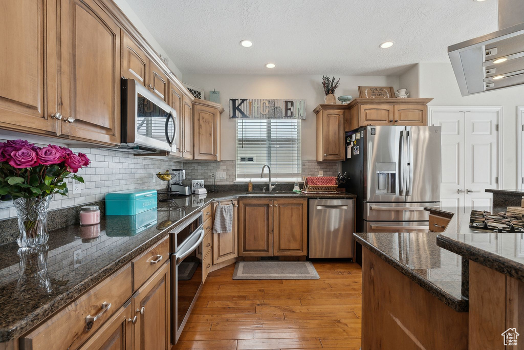 Kitchen featuring decorative backsplash, appliances with stainless steel finishes, a sink, dark stone countertops, and light wood-type flooring