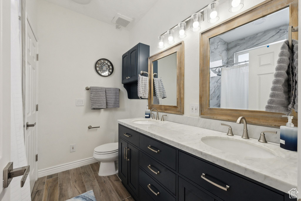 Full bath with toilet, double vanity, a sink, and wood finished floors