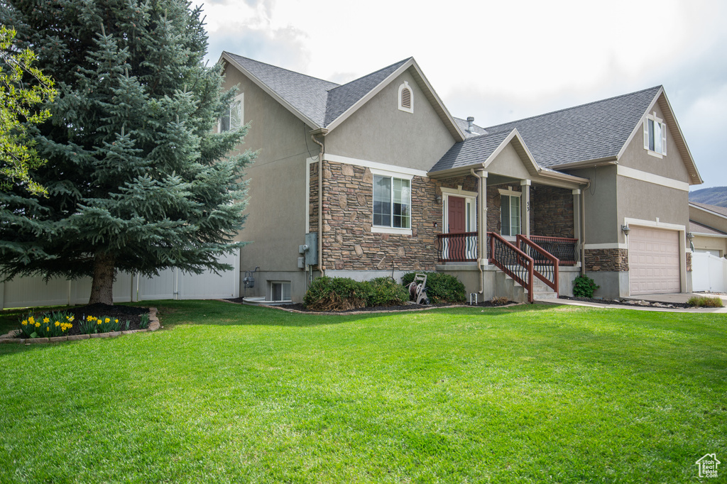 View of front of property featuring stucco siding, roof with shingles, a front lawn, and stone siding