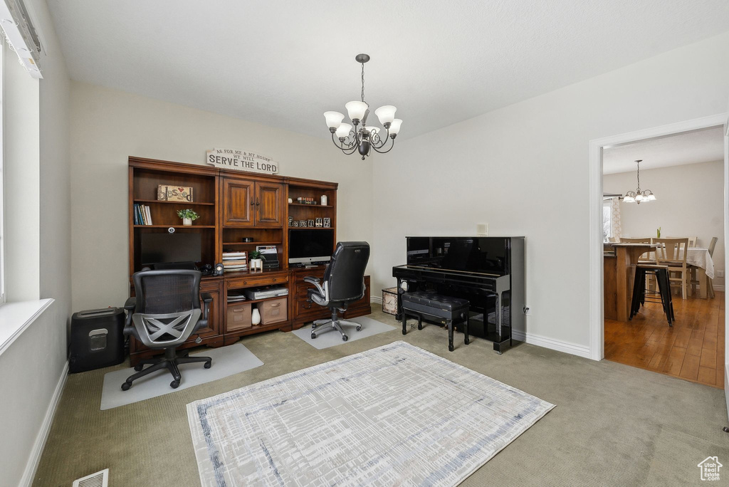Carpeted home office with baseboards, visible vents, and an inviting chandelier