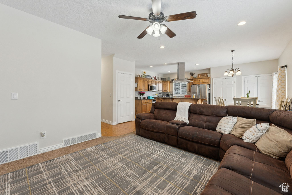 Living room featuring ceiling fan with notable chandelier, recessed lighting, visible vents, and baseboards