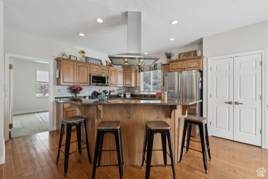 Kitchen featuring a center island, island exhaust hood, backsplash, appliances with stainless steel finishes, and a sink