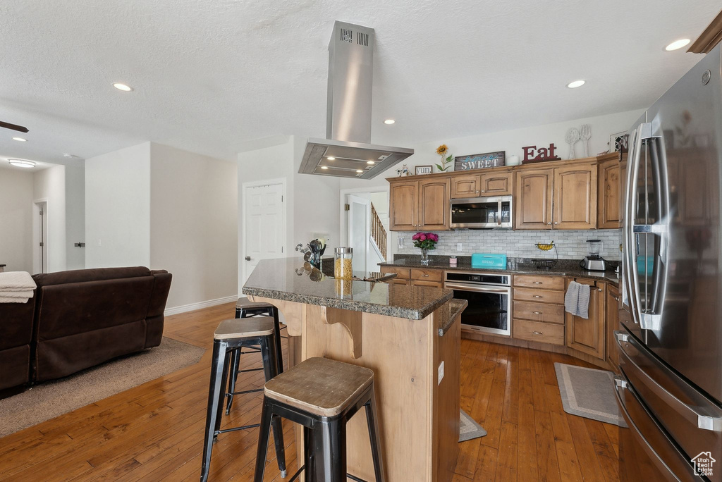 Kitchen with island range hood, dark countertops, a kitchen island, a breakfast bar area, and stainless steel appliances