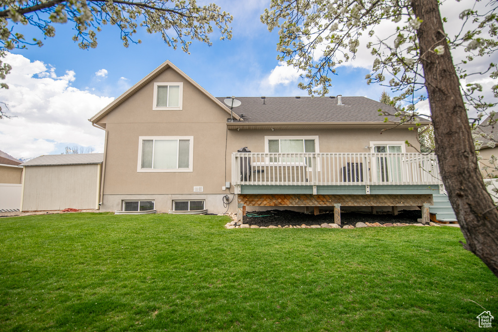 Rear view of house featuring a lawn, roof with shingles, a deck, and stucco siding