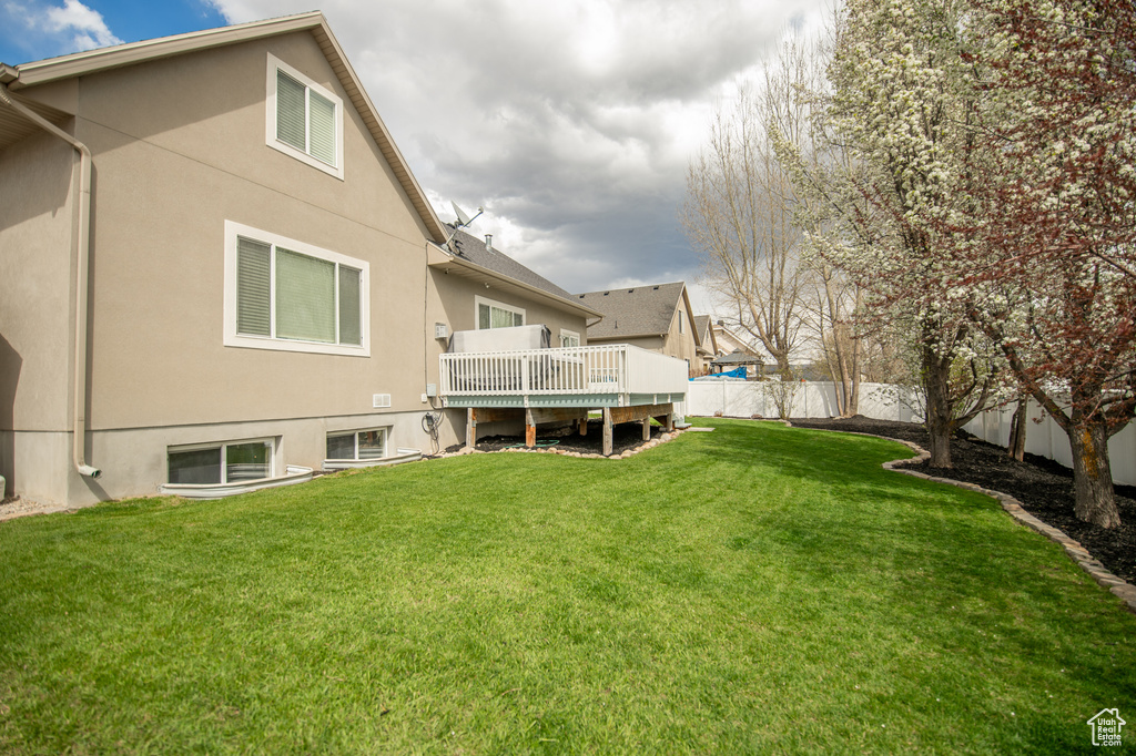 Rear view of property with stucco siding, a deck, a yard, and a fenced backyard