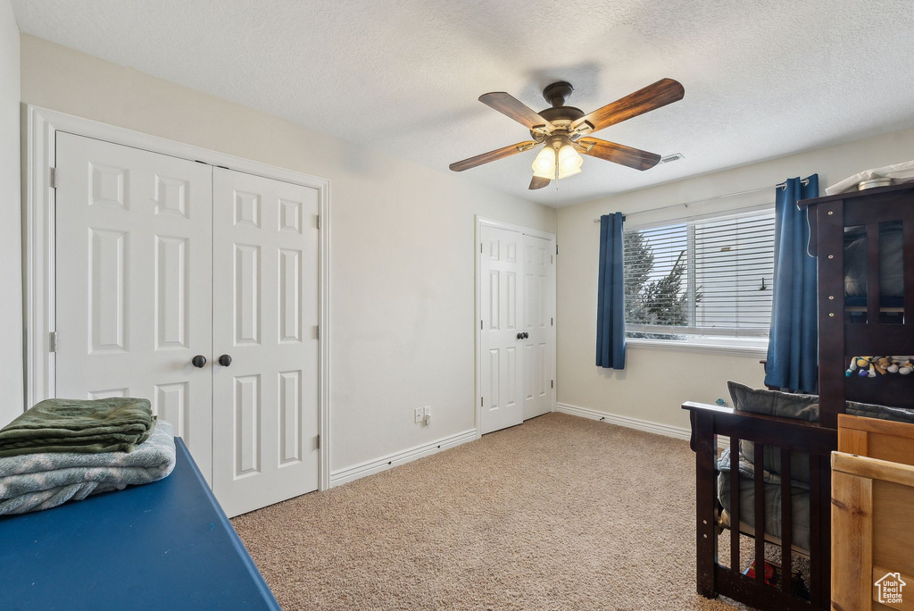 Carpeted bedroom featuring a ceiling fan, a textured ceiling, baseboards, and multiple closets