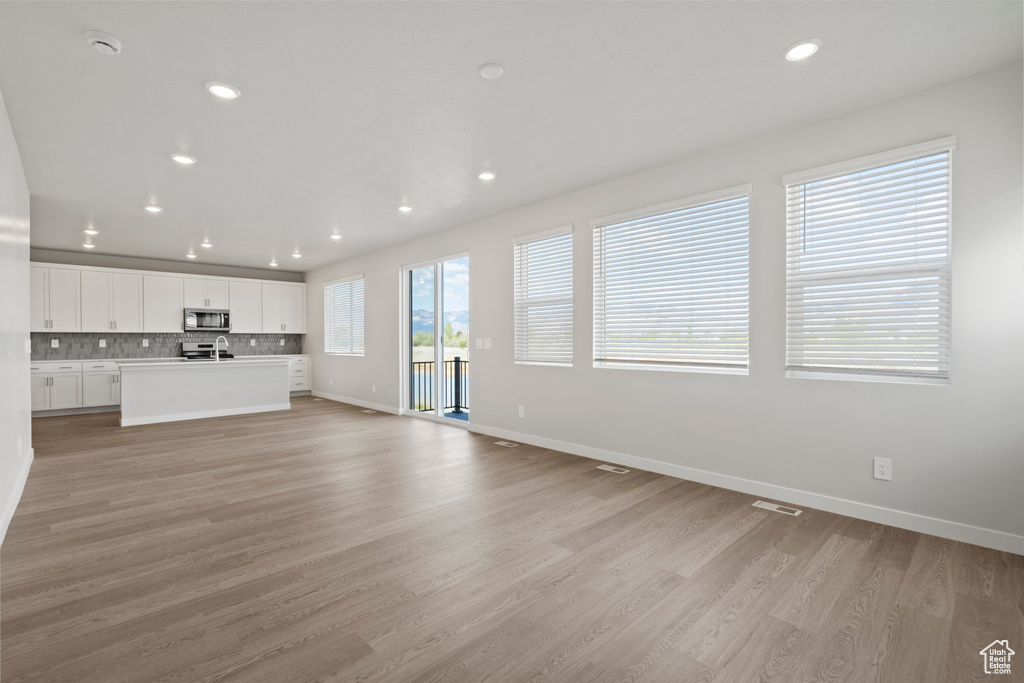 Unfurnished living room with visible vents, a sink, baseboards, light wood-style floors, and recessed lighting