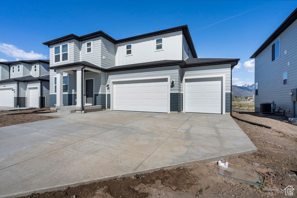 View of front of house with central air condition unit, an attached garage, and concrete driveway