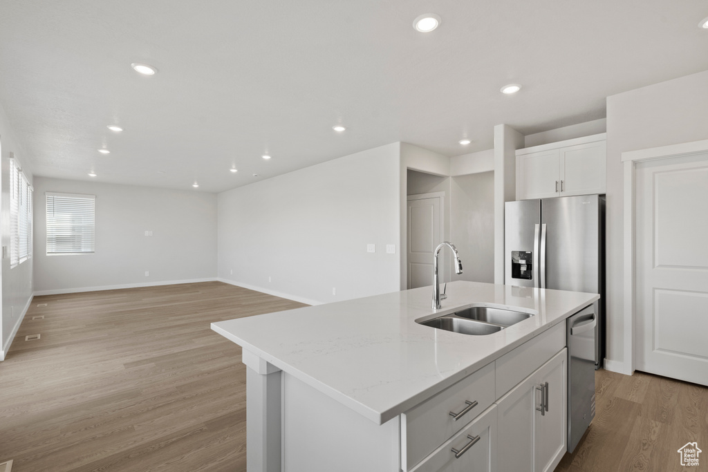 Kitchen featuring a sink, light wood-style floors, stainless steel appliances, white cabinetry, and a center island with sink