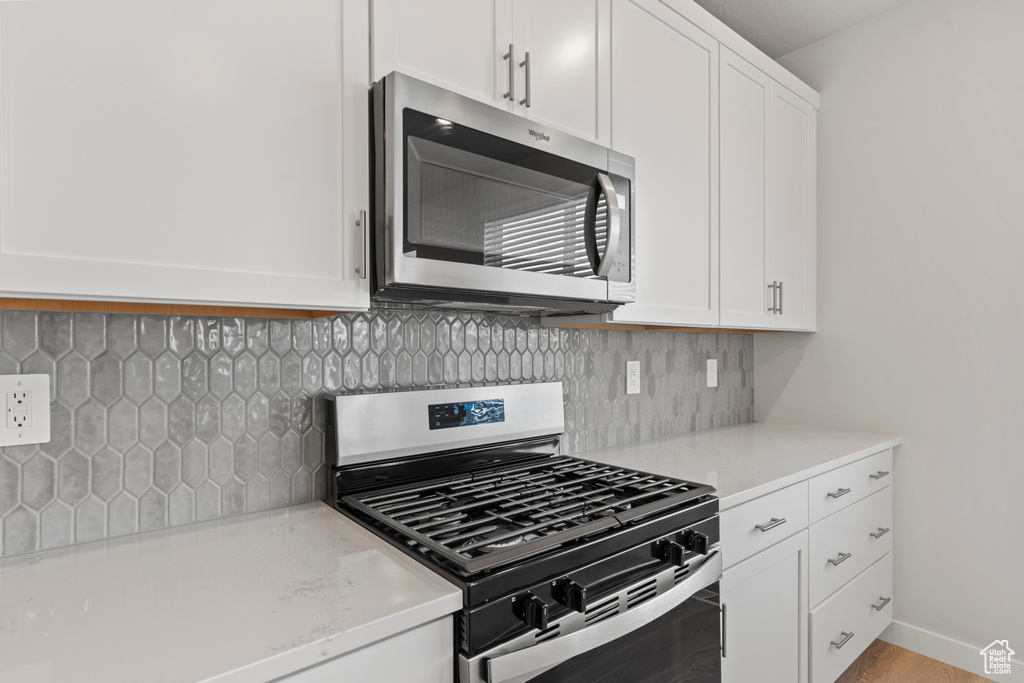 Kitchen with light stone counters, white cabinetry, appliances with stainless steel finishes, and tasteful backsplash