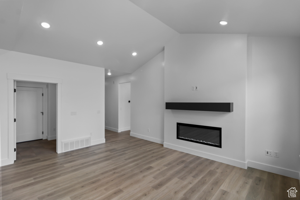 Unfurnished living room with recessed lighting, light wood-style floors, a glass covered fireplace, visible vents, and vaulted ceiling