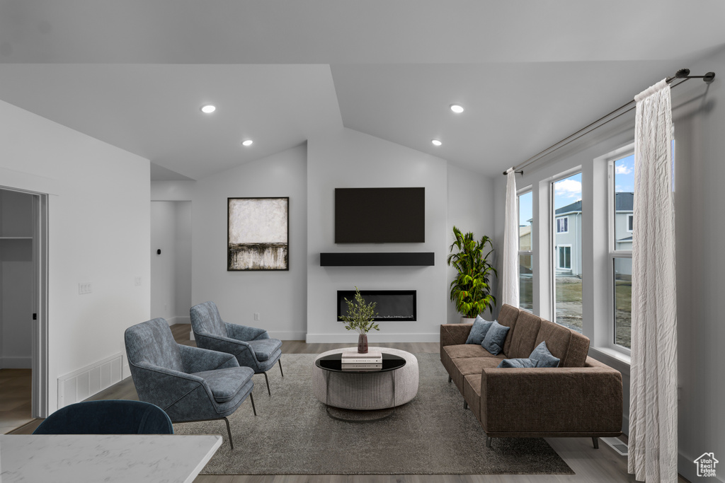 Living room featuring recessed lighting, lofted ceiling, wood finished floors, and a glass covered fireplace
