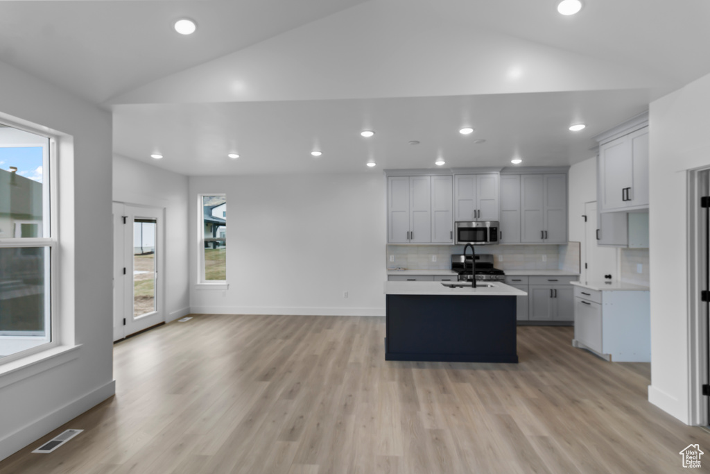 Kitchen featuring stainless steel microwave, light countertops, vaulted ceiling, visible vents, and a center island with sink