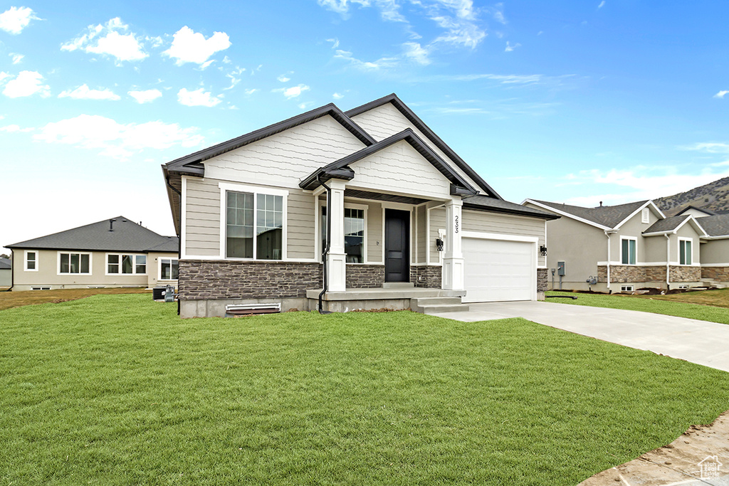 Craftsman house with a front yard, concrete driveway, and stone siding