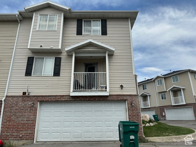 Multi unit property featuring brick siding, driveway, an attached garage, and a balcony