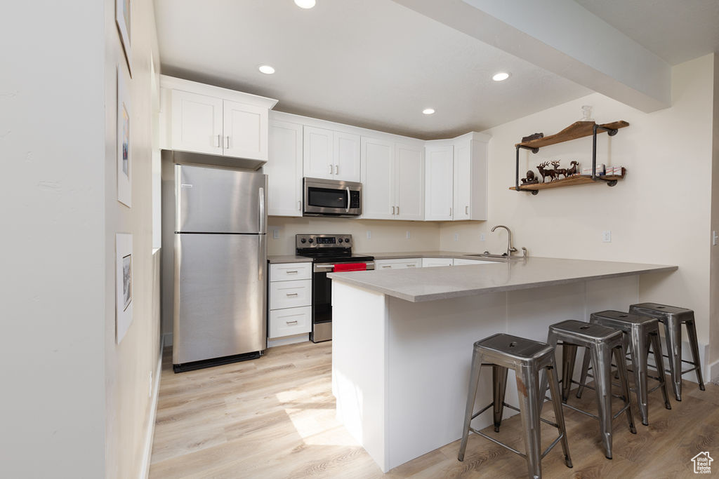 Kitchen with light wood-style flooring, a breakfast bar area, appliances with stainless steel finishes, a sink, and a peninsula