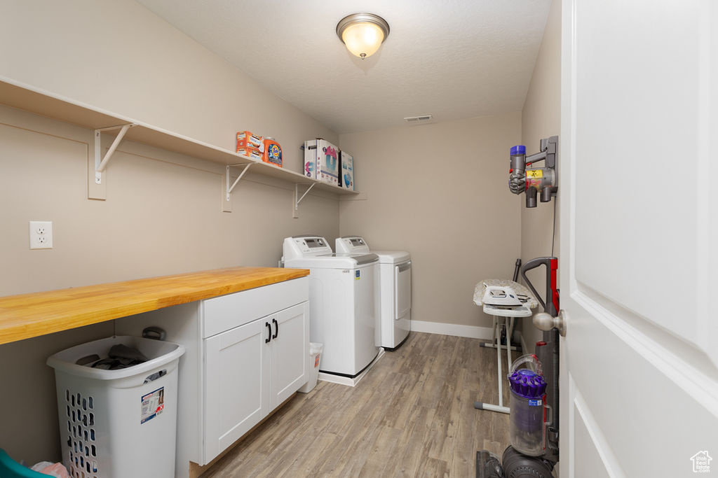 Clothes washing area with independent washer and dryer, visible vents, light wood-style floors, baseboards, and cabinet space