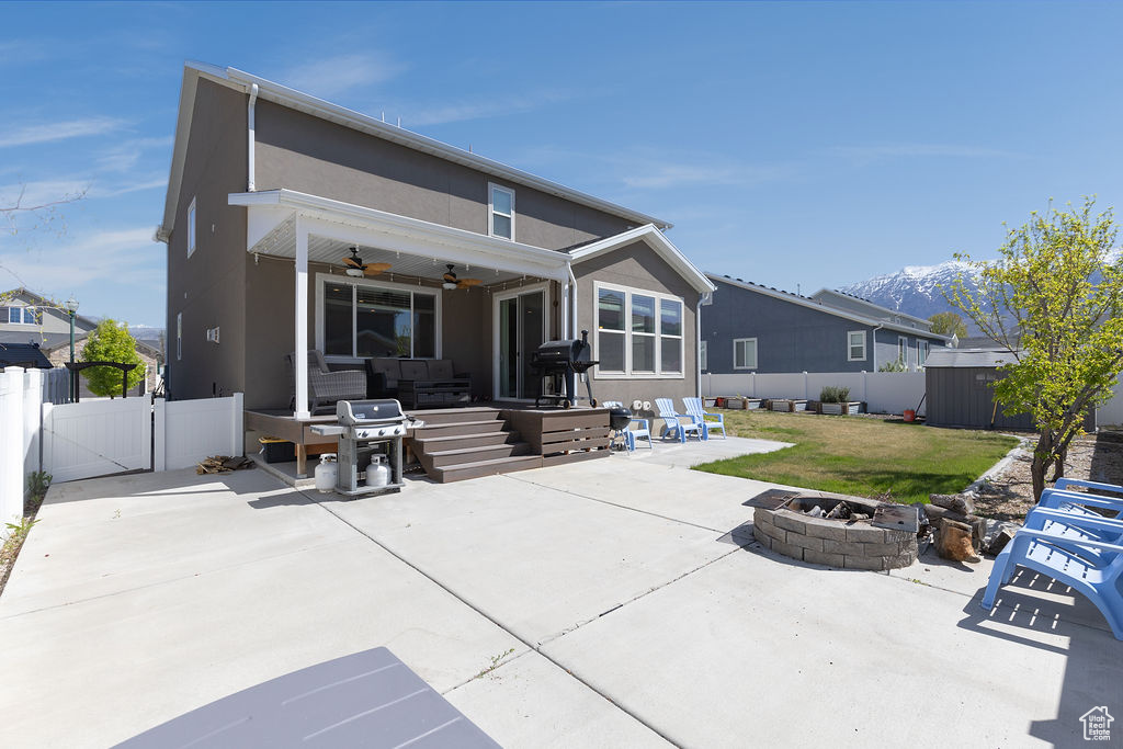 Rear view of property with a fenced backyard, a gate, ceiling fan, an outdoor living space with a fire pit, and a patio area