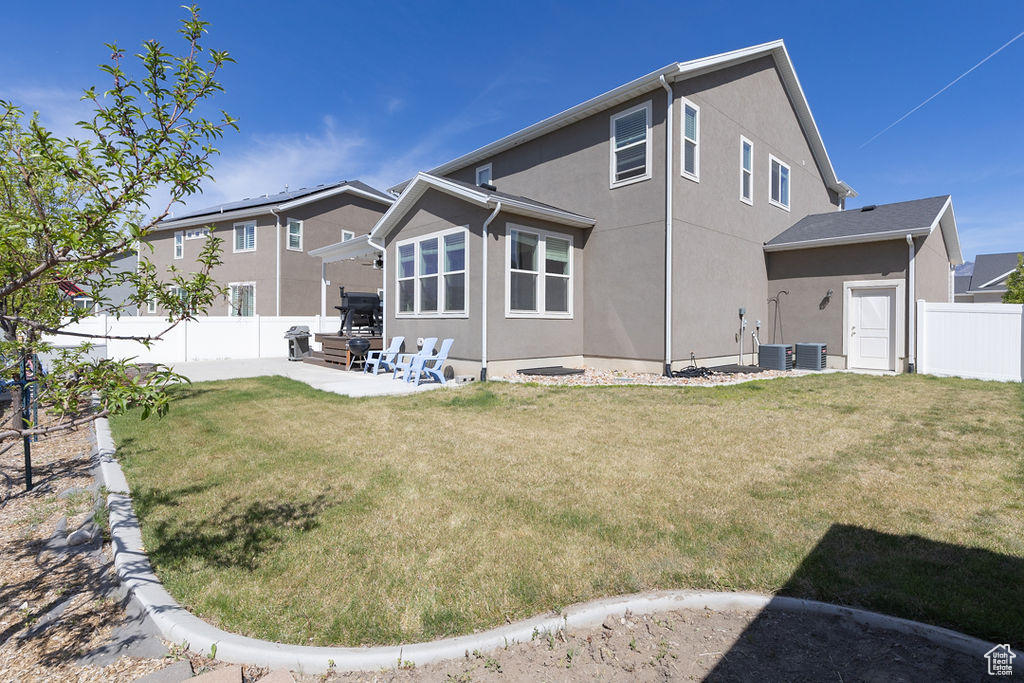 Rear view of house with fence, central AC unit, a yard, and stucco siding