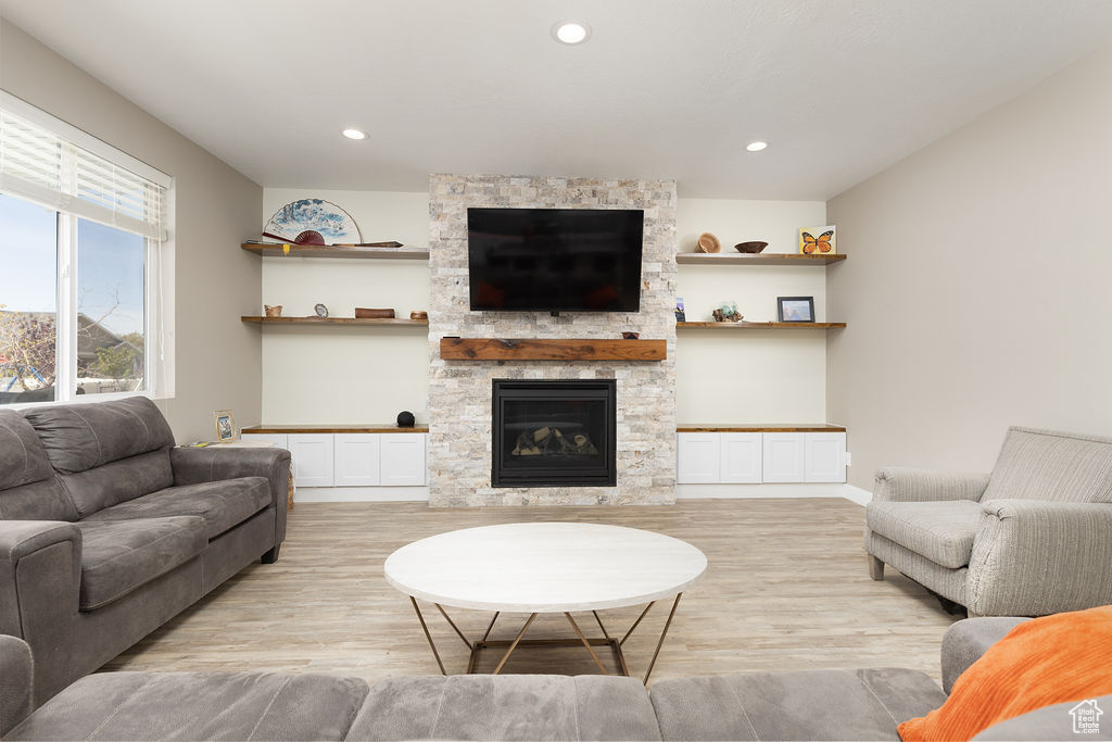 Living area with recessed lighting, a stone fireplace, and light wood-type flooring