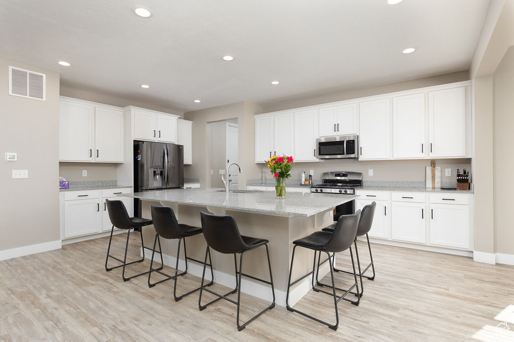 Kitchen featuring white cabinets, a sink, appliances with stainless steel finishes, visible vents, and an island with sink