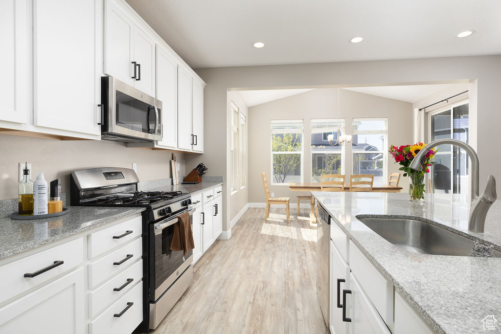 Kitchen with light stone countertops, light wood-style flooring, appliances with stainless steel finishes, a sink, and white cabinetry