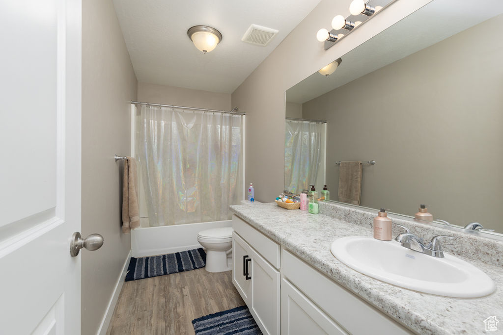 Full bathroom with vanity, toilet, visible vents, baseboards, and wood finished floors