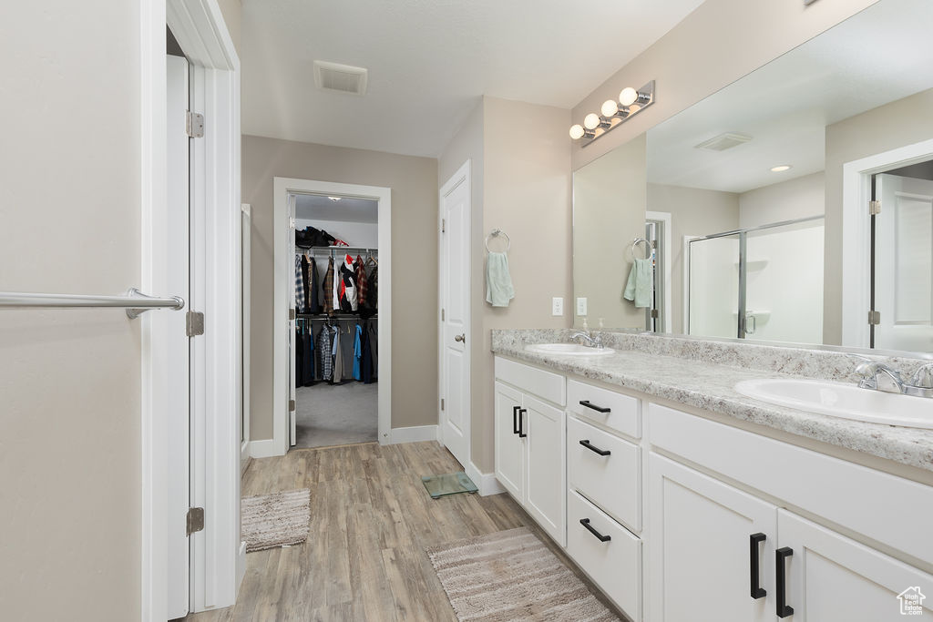 Full bathroom featuring a sink, a stall shower, double vanity, wood finished floors, and a spacious closet