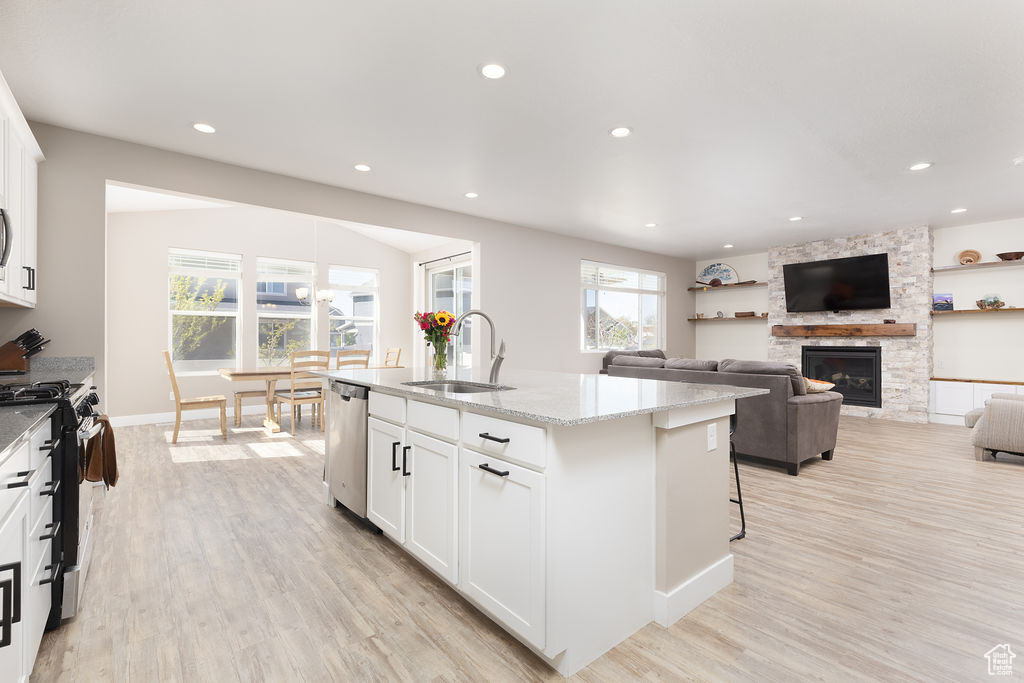 Kitchen with light wood finished floors, a sink, stainless steel appliances, a stone fireplace, and light stone counters