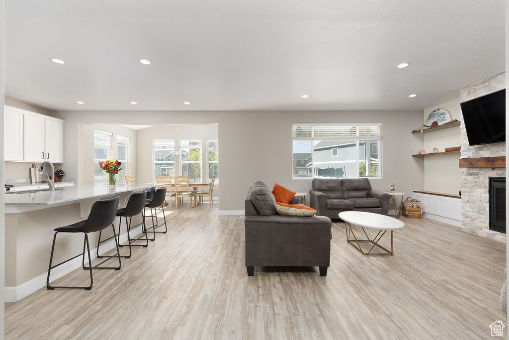 Living room with baseboards, light wood-type flooring, a stone fireplace, and recessed lighting