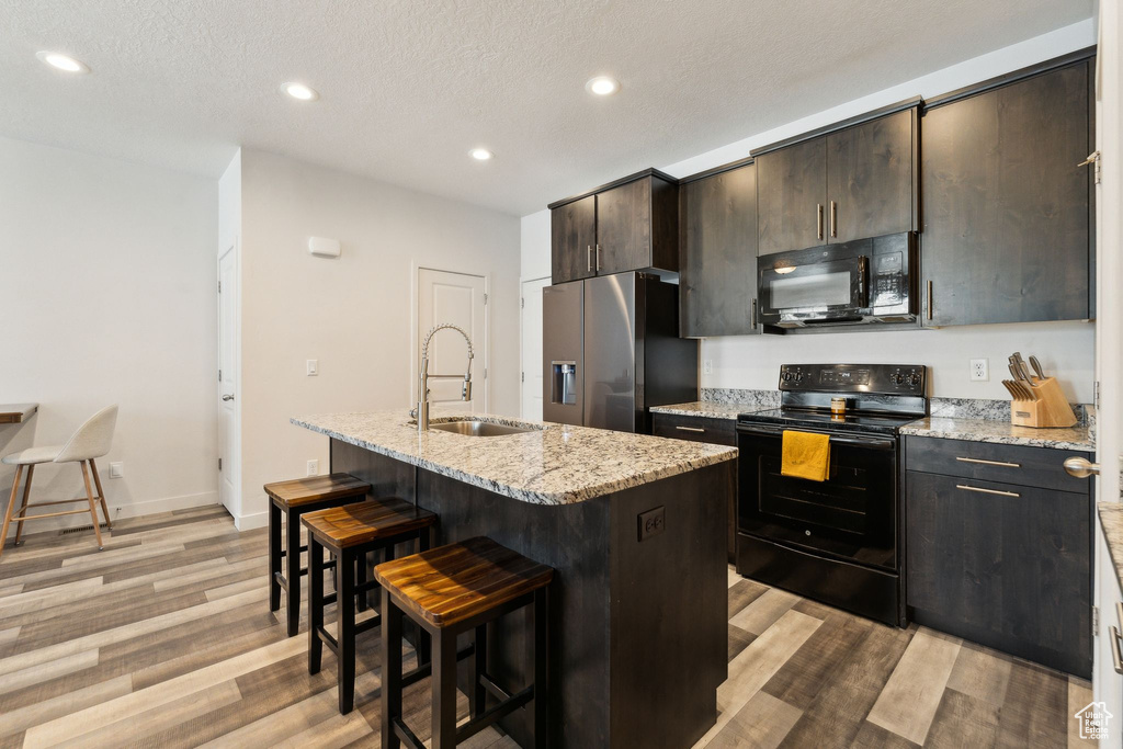 Kitchen featuring black appliances, a kitchen breakfast bar, light wood-style flooring, and a sink