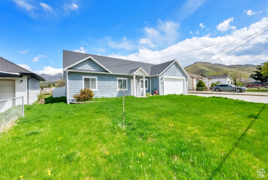 Ranch-style home featuring fence, a mountain view, a front lawn, and a garage