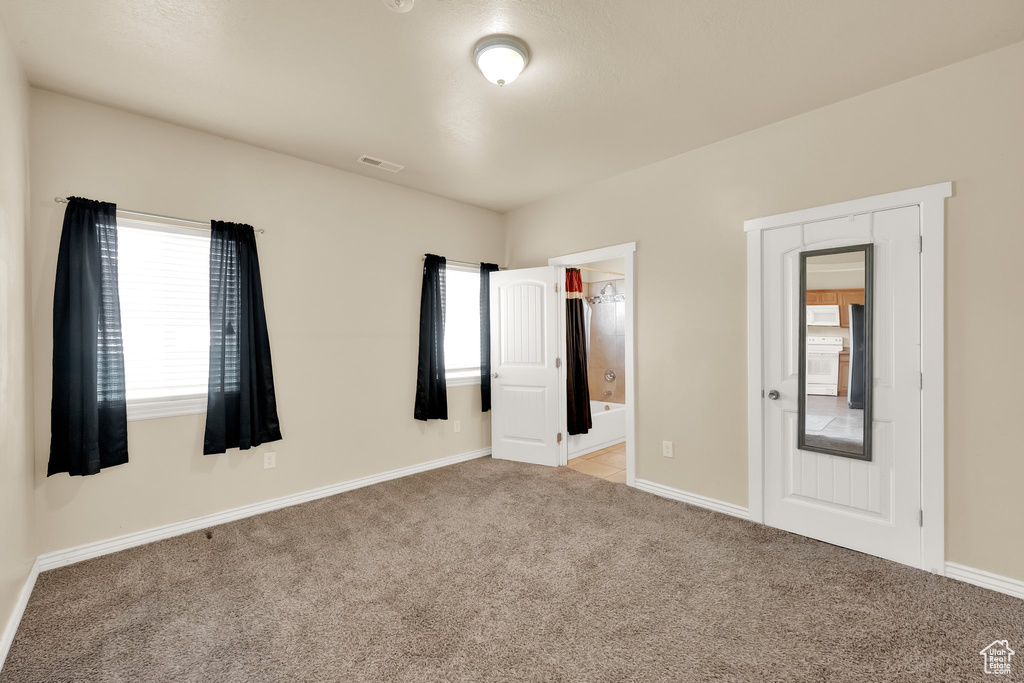 Unfurnished bedroom with baseboards, visible vents, connected bathroom, and light colored carpet
