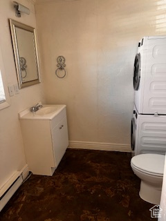 Bathroom with stacked washer / drying machine, baseboard heating, toilet, vanity, and baseboards