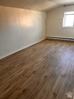 Additional living space with dark wood-style floors, baseboards, a textured ceiling, lofted ceiling, and a baseboard radiator