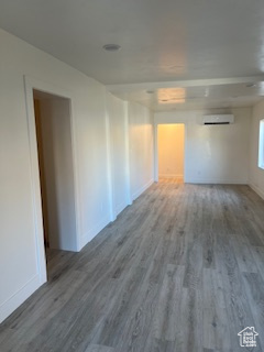 Unfurnished room featuring baseboards, a wall unit AC, and wood finished floors