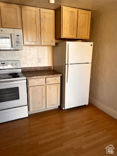 Kitchen with decorative backsplash, white appliances, baseboards, dark countertops, and wood finished floors