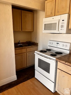 Kitchen with a sink, white appliances, dark wood-type flooring, light brown cabinetry, and baseboards