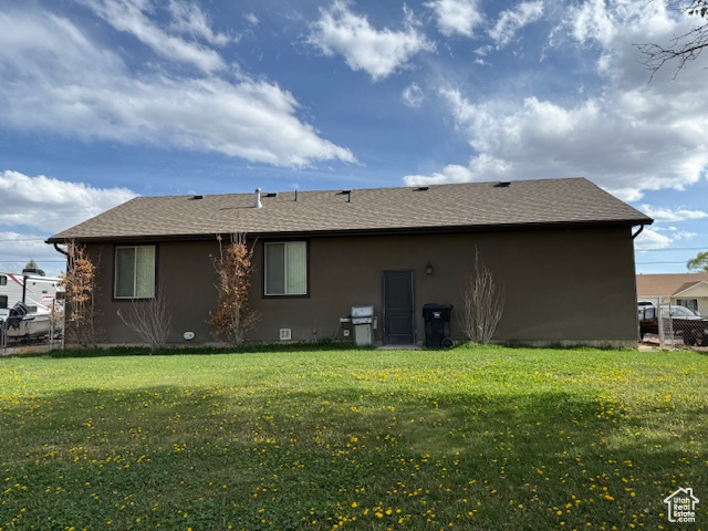 Back of house featuring fence, a yard, stucco siding, and roof with shingles