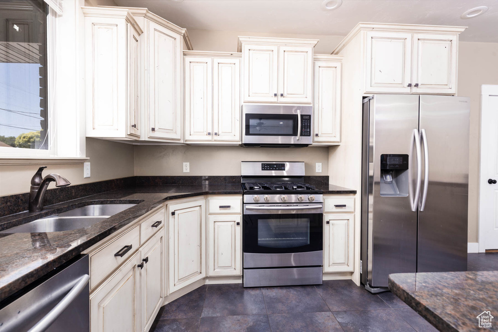 Kitchen featuring appliances with stainless steel finishes, a sink, and dark stone countertops
