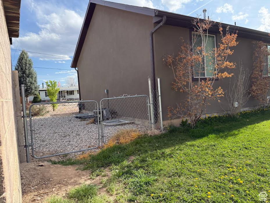View of side of home with a lawn, fence, stucco siding, and a gate